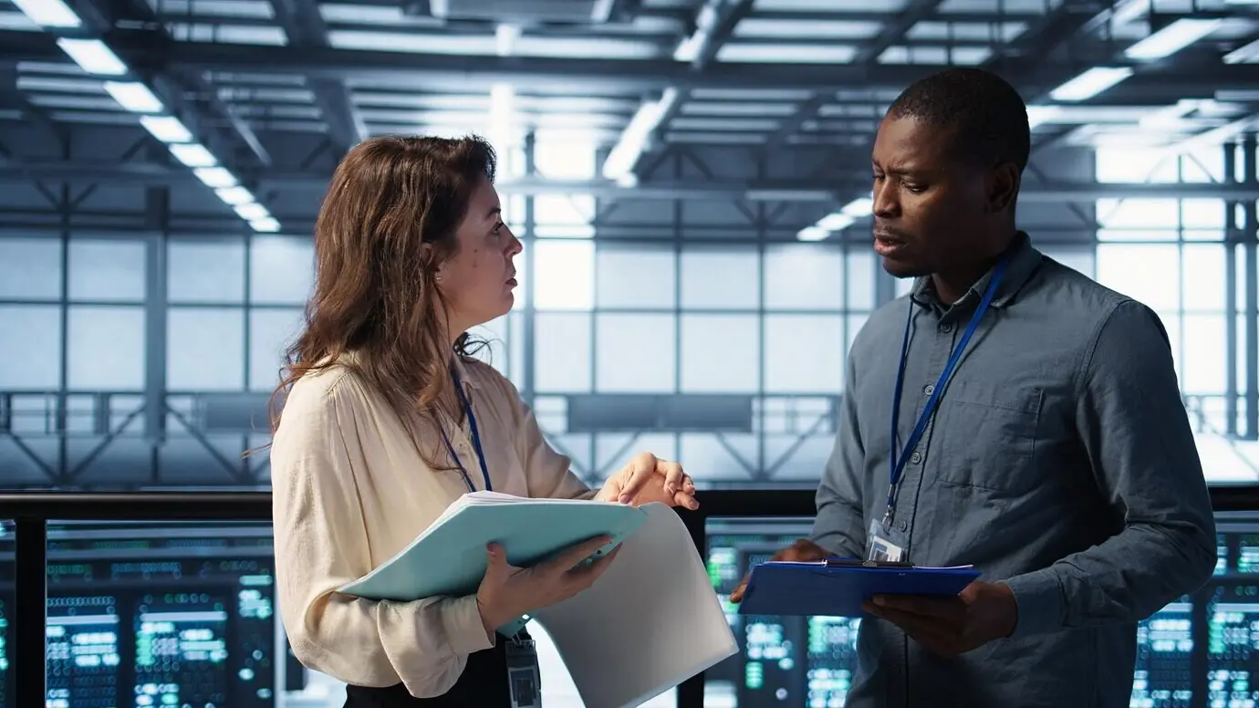 Administradores alegres se reúnen en un centro de datos para revisar informes y se dan la mano.